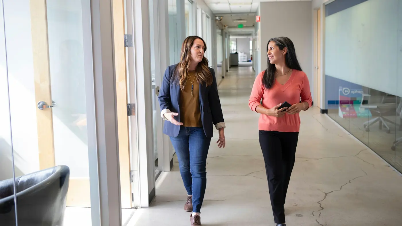 Two colleagues walking and talking together down an office corridor
