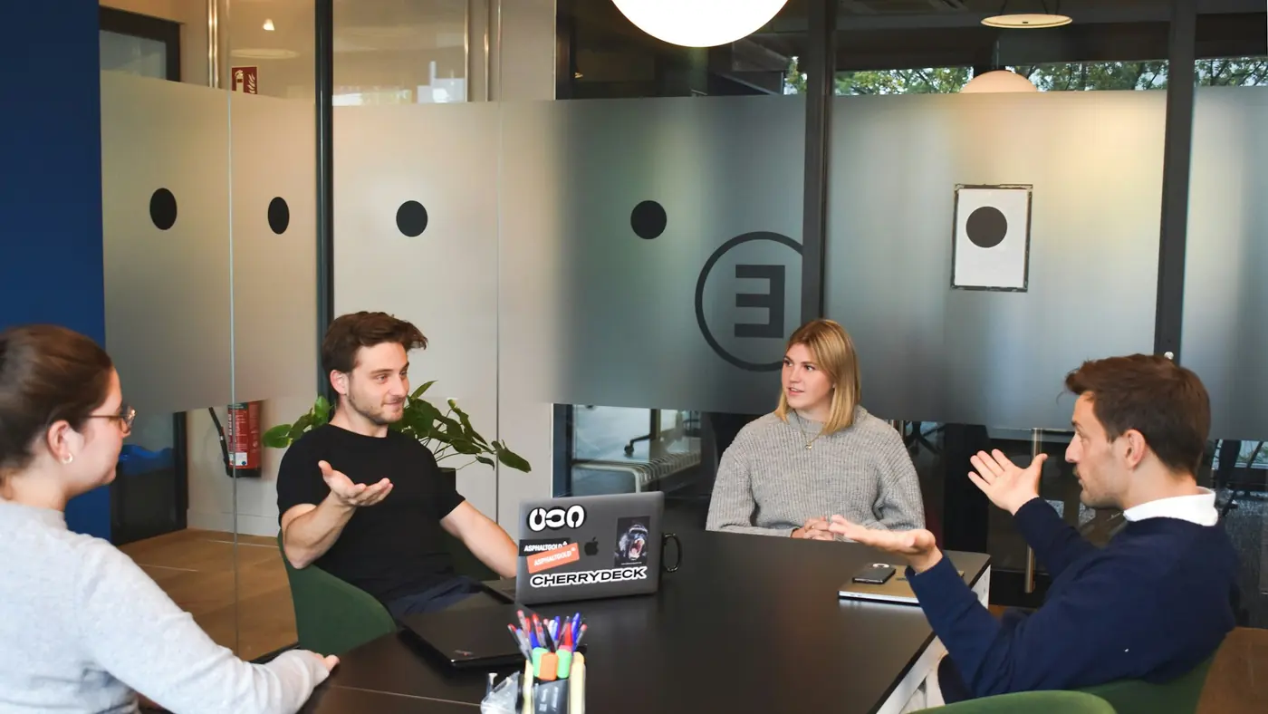 A team talking around a meeting table, one person explaining while the others listen